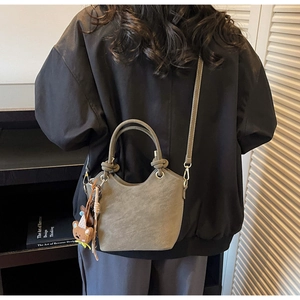Detail view of a matte leather bucket bag with a bear charm on a model shoulder