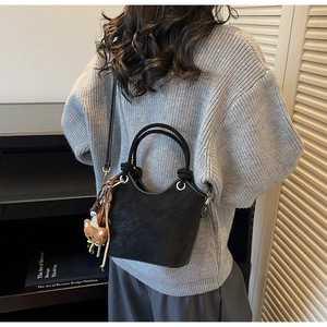 Detail of black matte bucket bag with white contrast stitching and a cute bear charm