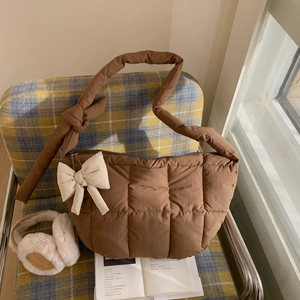 Détail d'un sac matelassé marron avec un grand nœud crème sur une chaise à carreaux