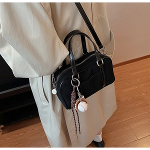 Dettaglio borsa bowling nera con ciondolo baseball su modella in trench coat beige
