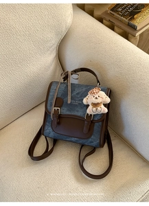 Detail of denim backpack with leather trim, featuring a cute plush puppy charm accessory