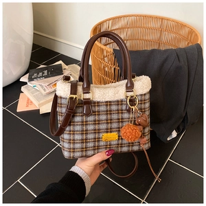 Detail der karierten Eimertasche mit weißem Plüschbesatz und orangefarbenem Bommel