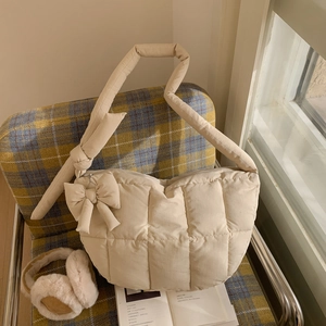 Détail du sac hobo matelassé crème avec un grand nœud décoratif et une ambiance hivernale