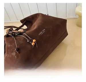 Detail of dark brown matte leather tote bag featuring drawstring and wood bead charms