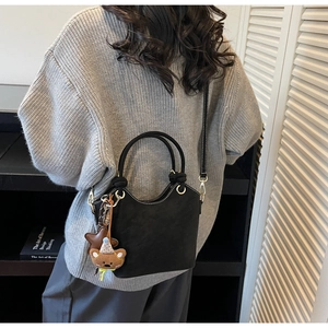 Detail of a black matte bucket bag with white contrast stitching and a cute bear charm