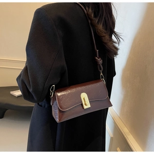 Gros plan du sac baguette en cuir marron vintage avec boucle dorée sur un manteau noir