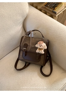 Detailed view of a vintage brown leather backpack on a beige sofa with a plush dog charm