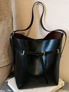 Minimalist black leather bucket bag with gold hardware buckle and spacious brown interior