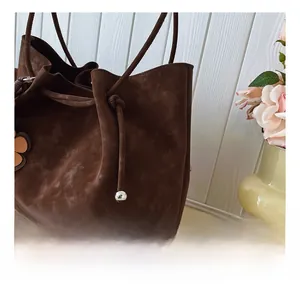 Detail of dark brown suede tote bag featuring a drawstring closure and a flower charm