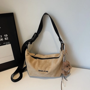 Detail of beige suede hobo bag featuring black branding and brown plush puppy charm