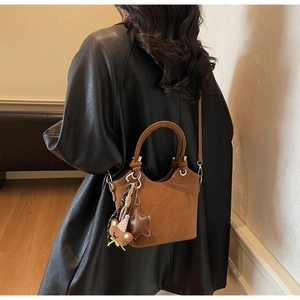 Close-up of brown suede bucket bag with cute bear charm and adjustable strap on a leather coat