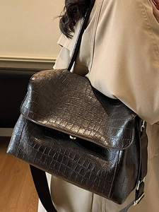 Classic dark brown crocodile embossed flap shoulder bag with a wide strap on a khaki trench coat