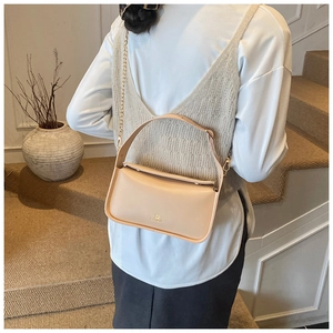Détail du sac baguette en cuir beige avec chaîne dorée et poignée porté par le modèle
