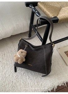 Gros plan d'un sac hobo marron foncé avec surpiqûres blanches et charme d'ours