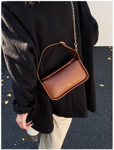 Détail d'un sac bandoulière en cuir marron avec chaîne dorée sur un manteau d'hiver noir