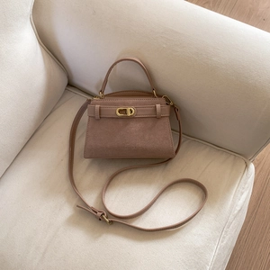 Detail view of pink suede crossbody bag with gold buckle and adjustable strap on sofa