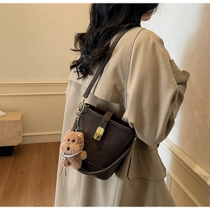 Détail du sac seau marron foncé avec fermoir doré et accessoire de charme ours en peluche