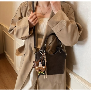 Detail of dark coffee bucket bag featuring plush bear and leather star charm pendants