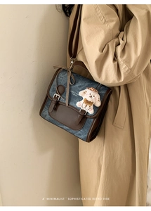Detail of blue denim retro crossbody bag with brown leather trim and puppy plush charm