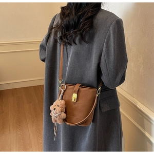 Détails d'un sac seau en cuir marron avec fermoir tournant doré et charm ours en peluche