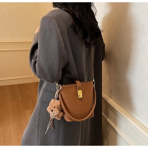 Détail du sac seau en cuir marron foncé avec fermoir doré et breloque ours en peluche