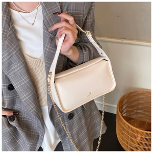 Détail du sac bandoulière en cuir beige élégant avec chaîne dorée et logo de la marque