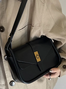 Borsa a tracolla nera minimalista in pelle con fibbia dorata su un trench elegante