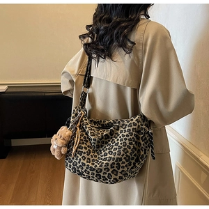 Detail of leopard print crossbody bag with plush bear charm worn over a beige trench coat
