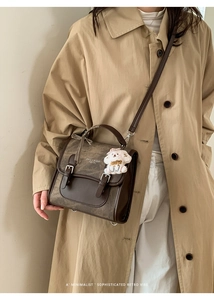 Detailed view of the brown retro flap backpack with dual metal buckles and plush charm