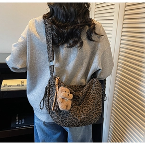 Detail view of leopard print hobo bag with a brown plush bear charm and adjustable strap