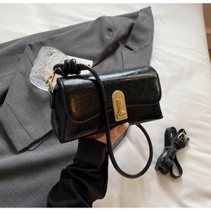 Détail du sac à bandoulière en cuir noir brillant avec fermoir rotatif doré et texture