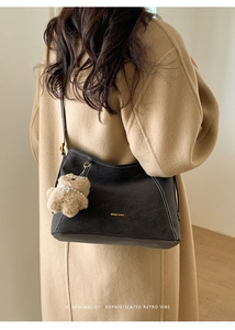 Détail d'un sac sous le bras marron mat avec coutures blanches et breloque ours