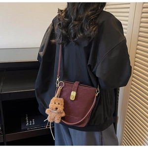 Gros plan d'un sac seau bordeaux vintage avec charm ours en peluche porté par un mannequin