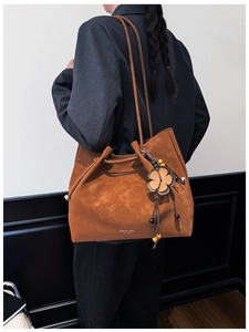 Detail of tan suede tote bag with decorative floral pendant and logo branding