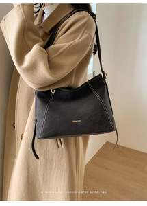 Détail d'un sac cabas en cuir noir avec surpiqûres blanches sur un manteau en laine