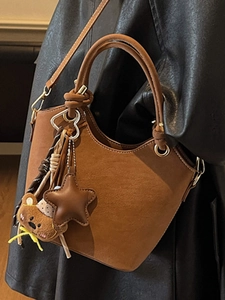 Brown suede bucket bag with cylinder handle and bear charm for casual crossbody wear