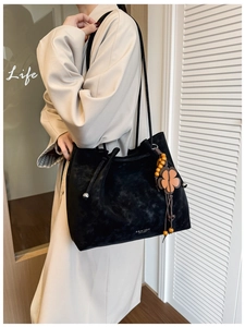 Detail of black suede tote bag with floral wooden bead charm and thin shoulder strap