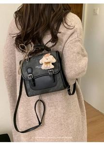 Detail of black leather backpack with dual buckles, bow accent, and cute puppy charm