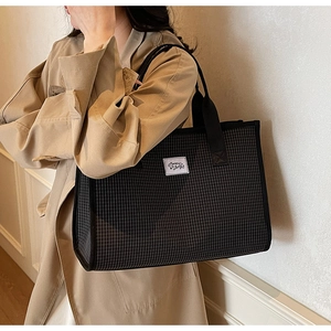 Close-up of classic black and white checkered tote bag worn with a khaki coat