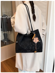 Close-up of black suede tote bag with silver logo and decorative flower charm detail