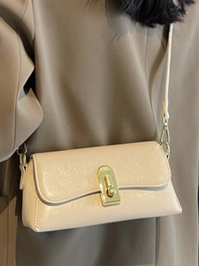 Petit sac bandoulière beige brillant avec fermoir doré porté sur un blazer marron élégant