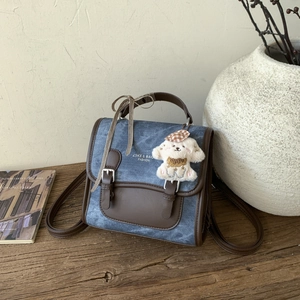 Detail of denim blue canvas backpack with leather straps and a cute dog plush charm
