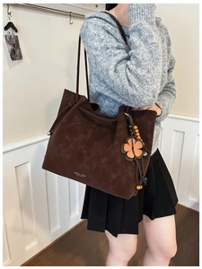 Detail of dark brown suede tote bag with leather flower charm and silver logo