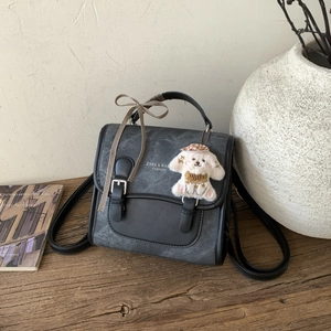 Detail of gray vintage backpack with decorative plaid bow and plush dog charm on desk