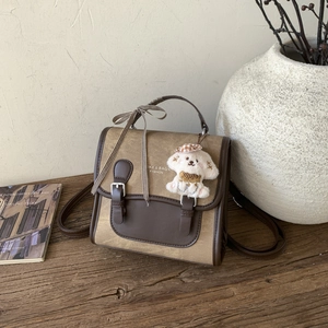 Detail view of khaki canvas and brown leather backpack with cute dog plush keychain and bow
