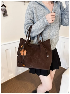 Close-up of a dark brown suede tote bag with flower charm and wooden bead tassel detail