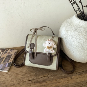 Detail of green canvas crossbody bag with brown leather trim and a cute puppy plush charm