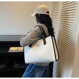 Rear view of a model wearing a large cream tote bag with black trim and wide straps