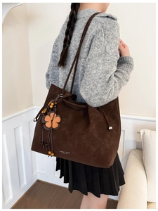 Detail view of large brown suede tote bag with floral charm and fringe hanging on shoulder