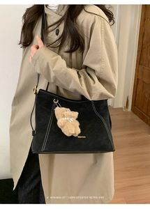 Détail du sac fourre-tout en daim noir avec surpiqûres blanches et pendentif ours
